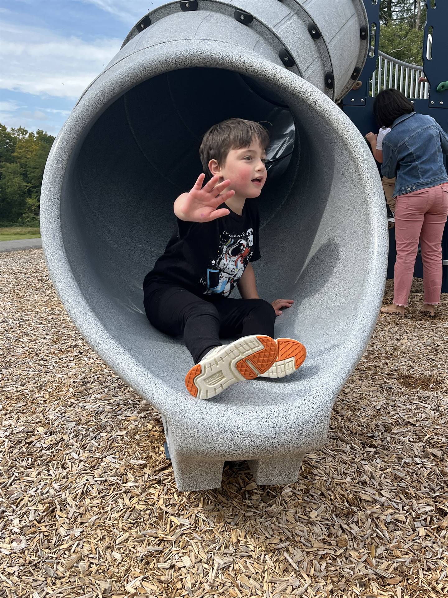 student sliding out of a slide & waving