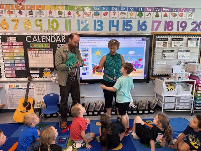 1 adult with octopus puppet and 1 adult with heart and students watching