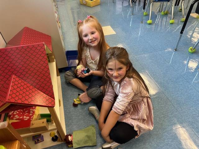 2 students are playing in a doll house with a red roof. 