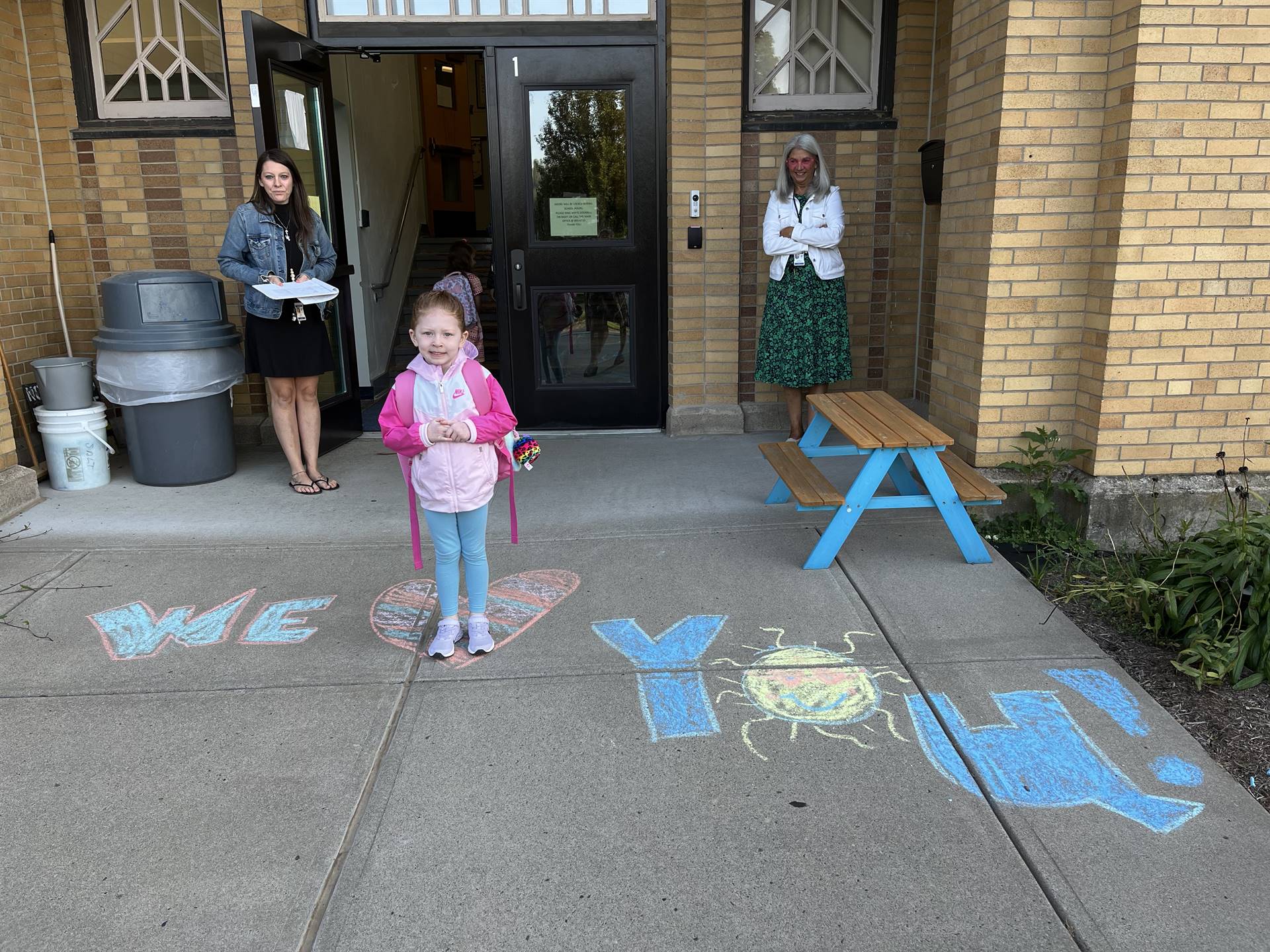 student standing on a sidewalk chalk heart in front of a school doorway