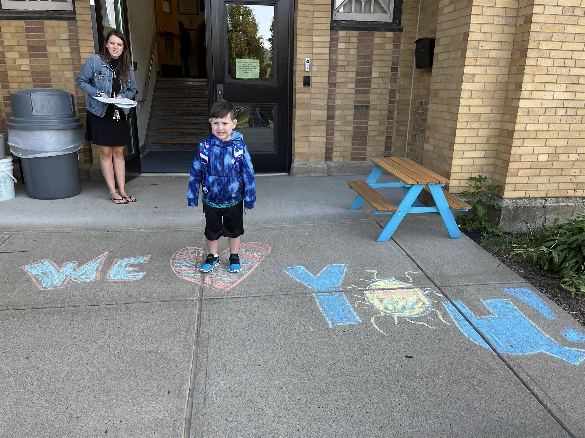 student standing on a sidewalk chalk heart in front of a school doorway