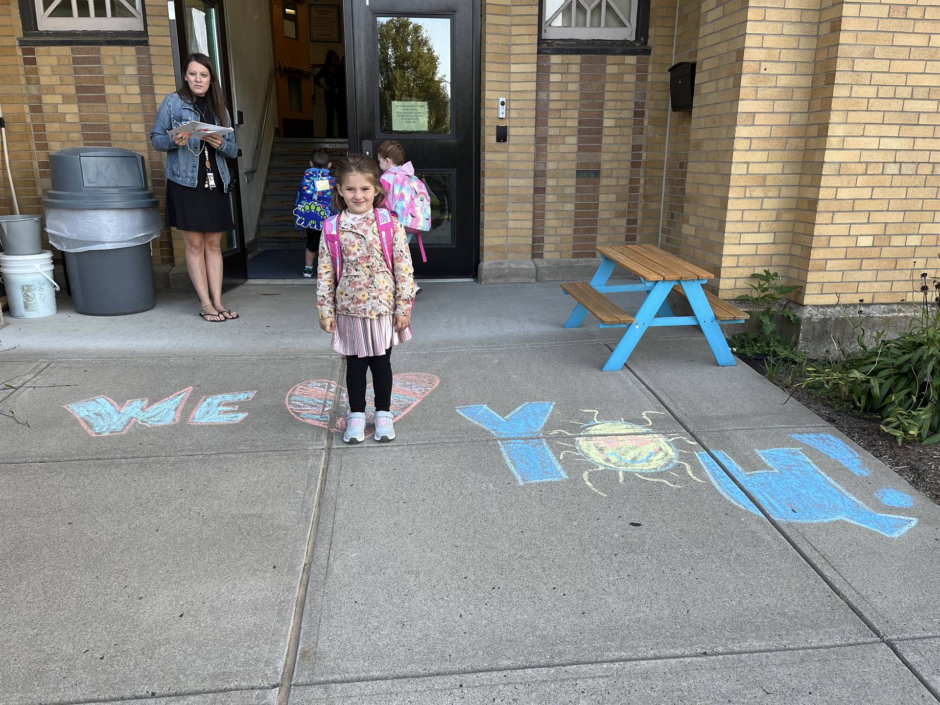 student standing on a sidewalk chalk heart in front of a school doorway