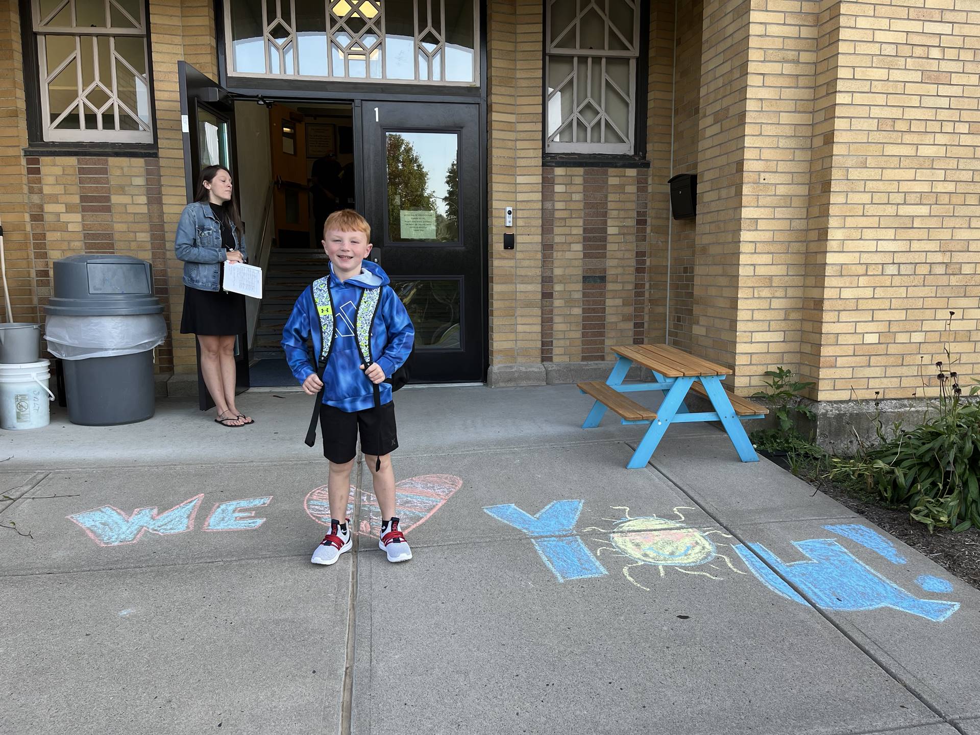 student standing on a sidewalk chalk heart in front of a school doorway