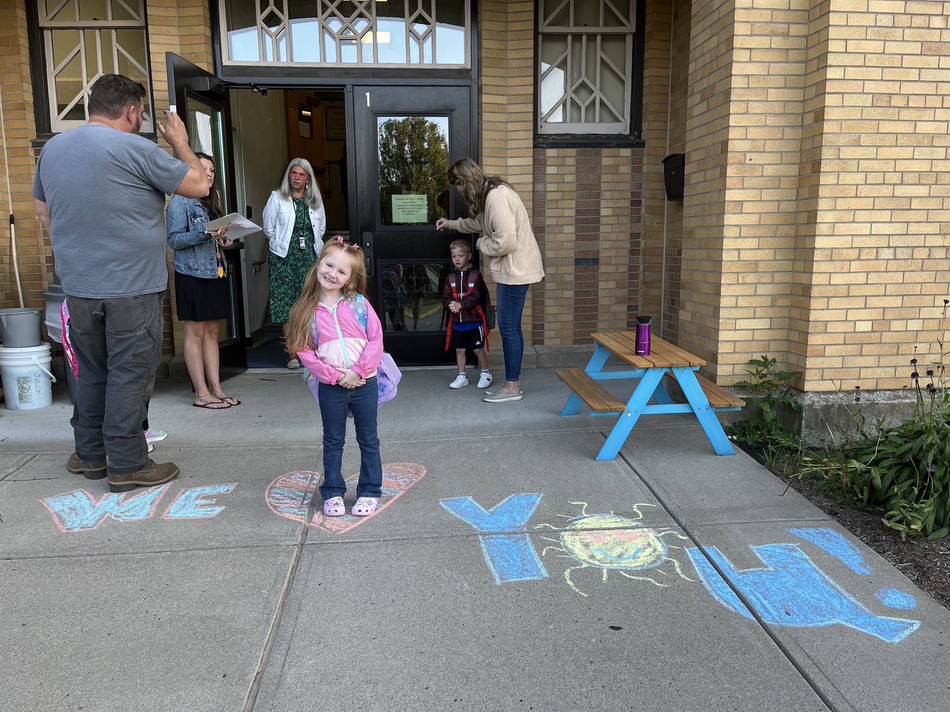 student standing on a sidewalk chalk heart in front of a school doorway 