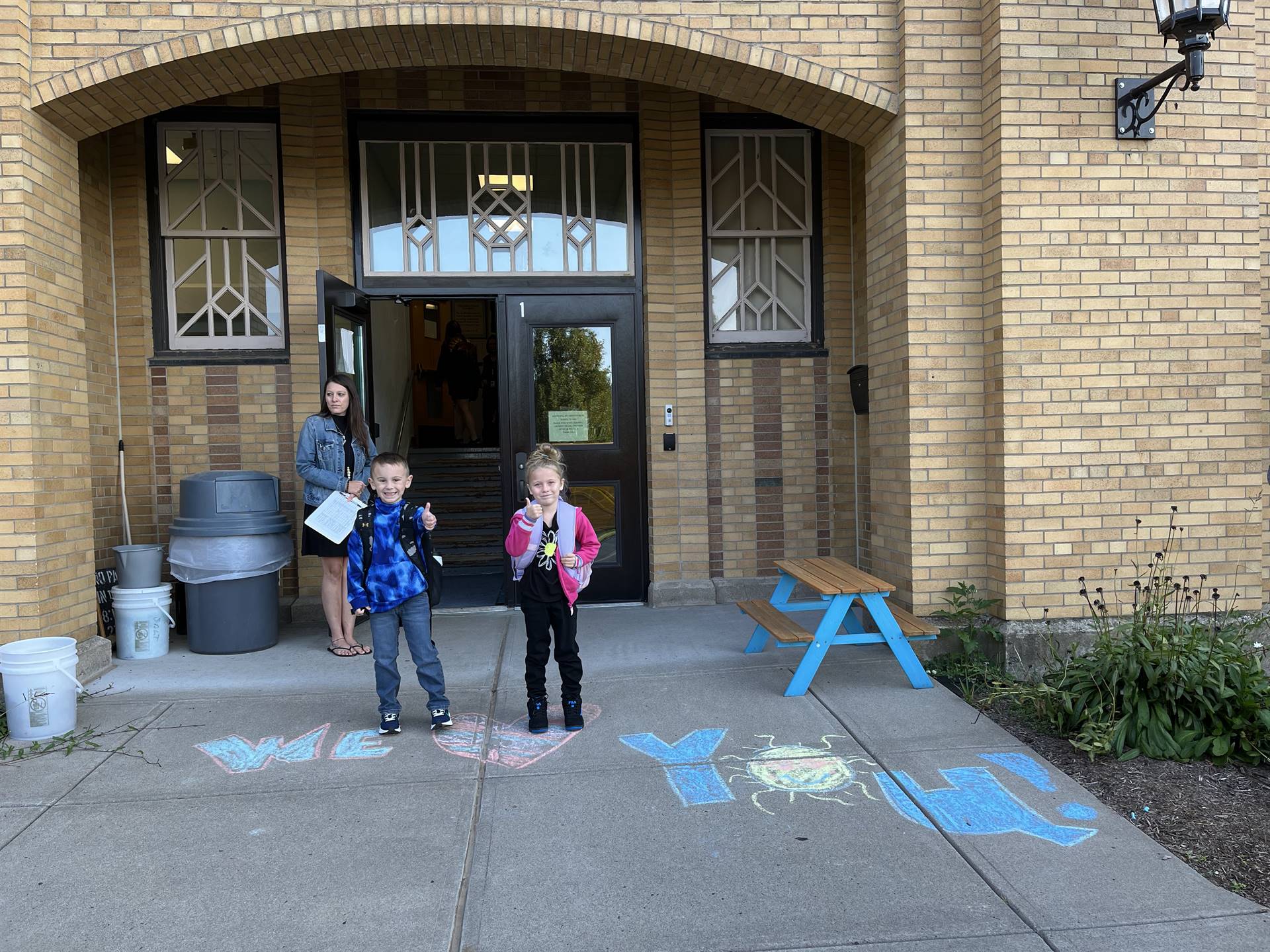 2 students standing on a sidewalk chalk heart in front of a school doorway