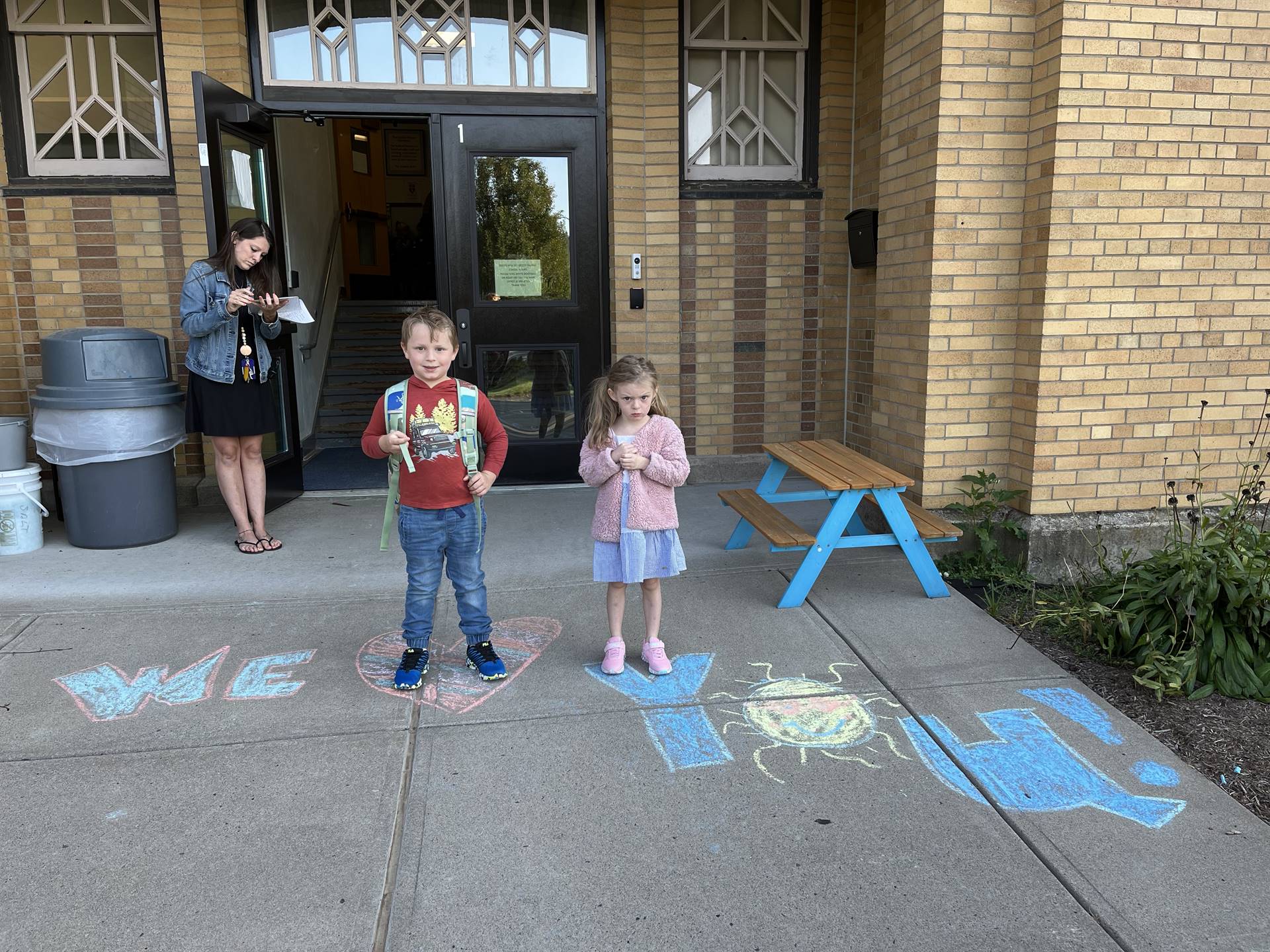 2 students standing on a sidewalk chalk heart in front of a school doorway