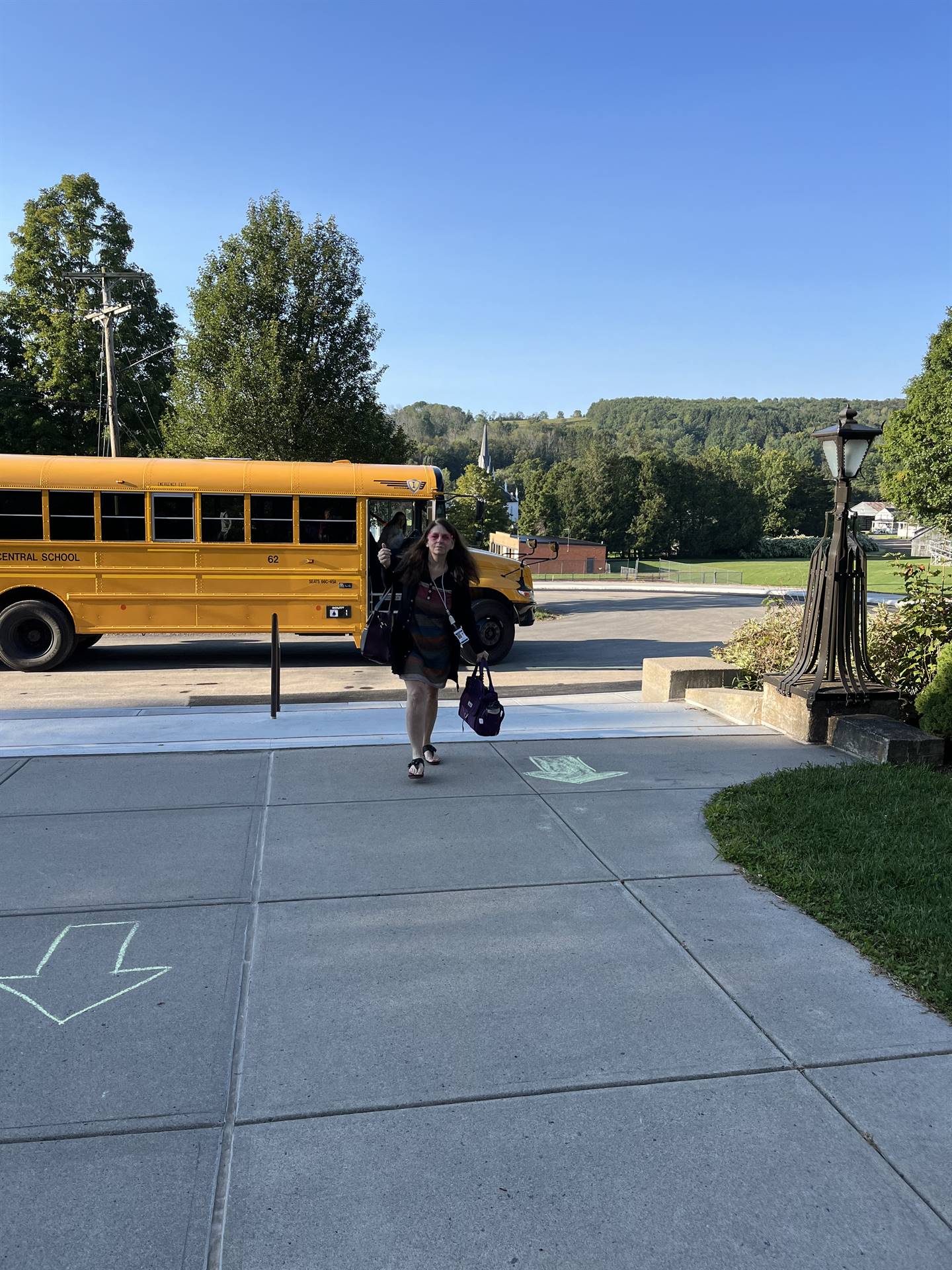 adult coming down sidewalk. school bus in background.