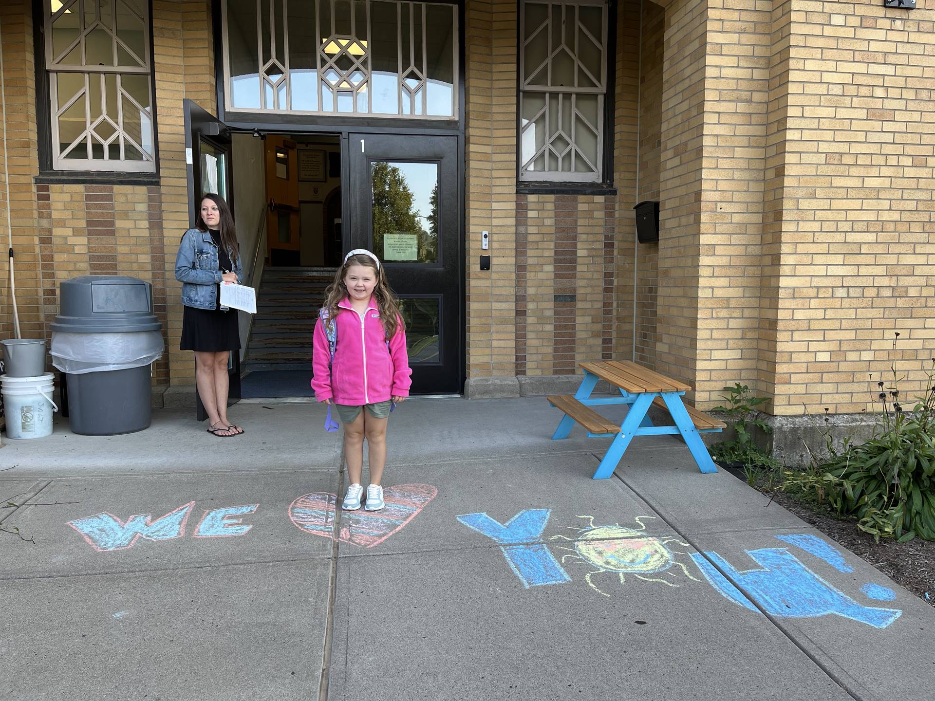 student standing on a sidewalk chalk heart in front of a school doorway