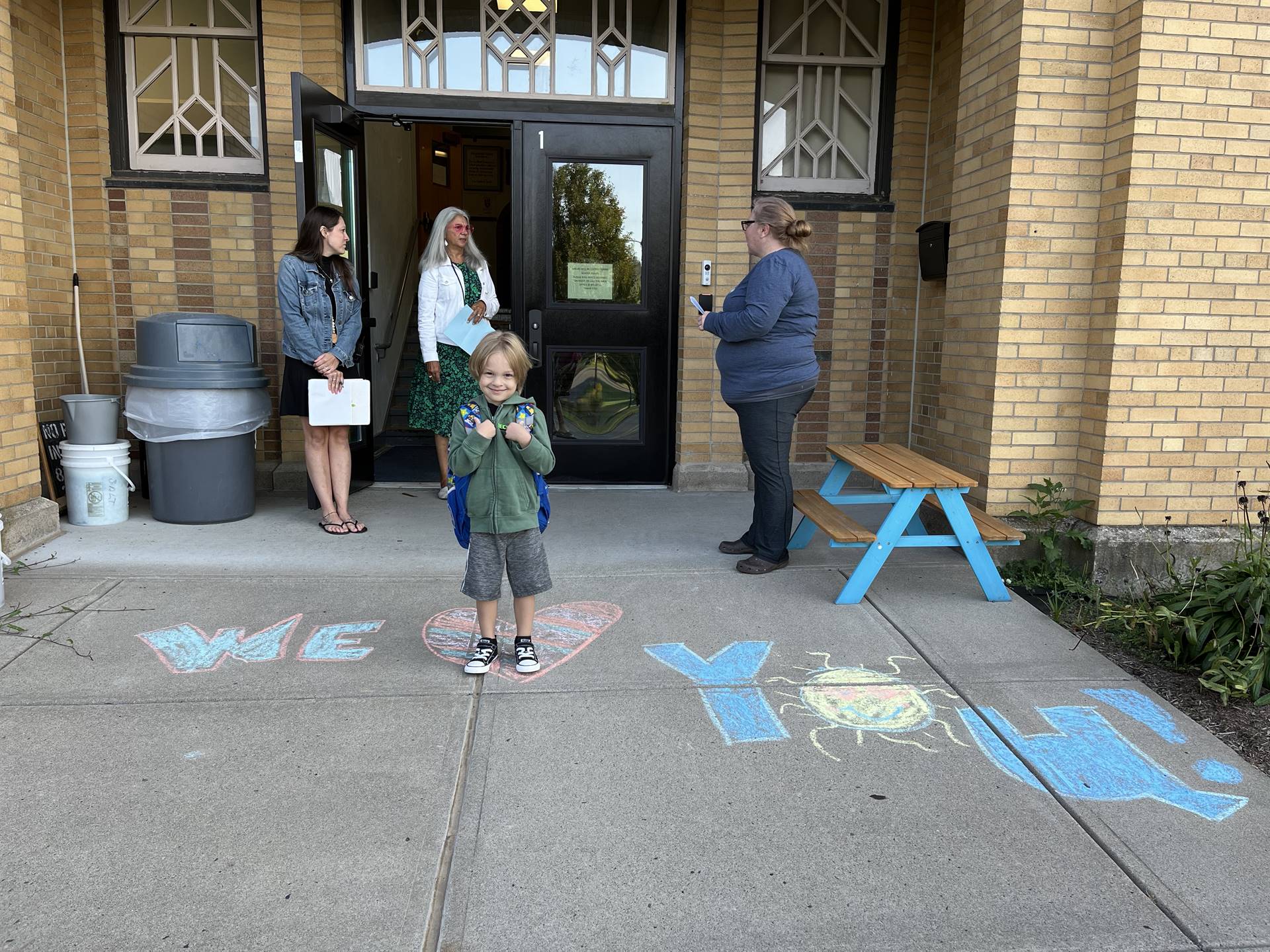 student standing on a sidewalk chalk heart in front of a school doorway