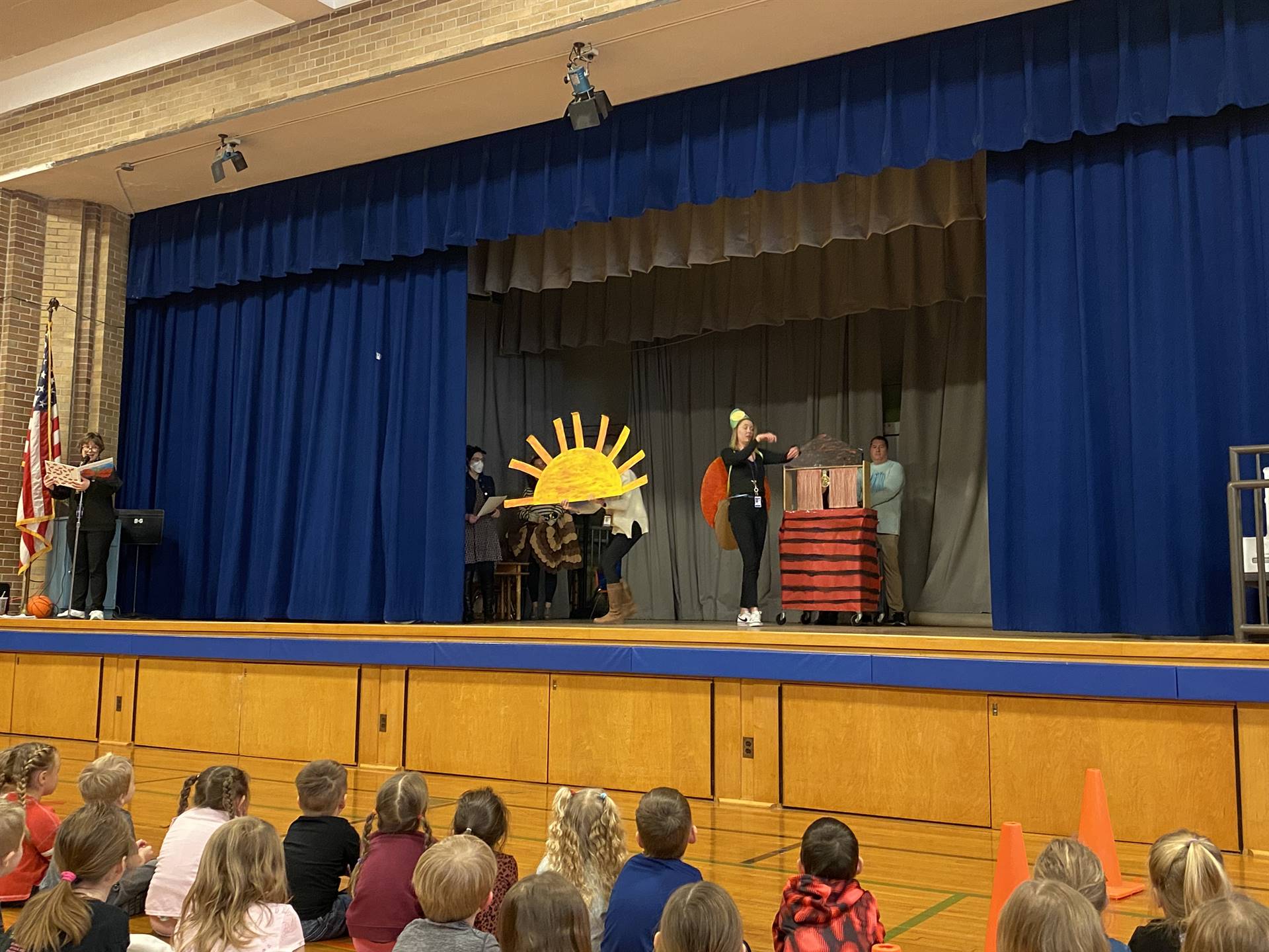 A person with a cardboard sun, a dressed up firefly and a red house with black stripes