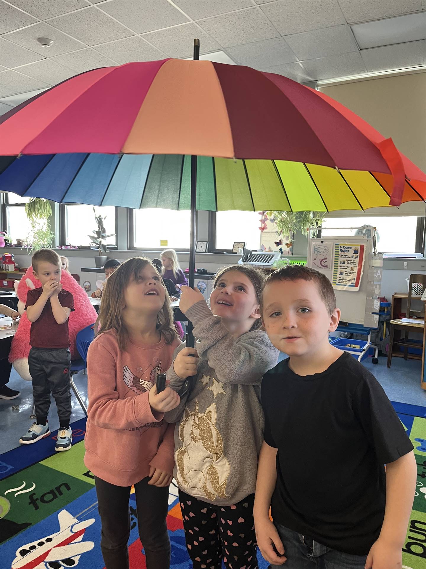 3 students under a rainbow umbrella