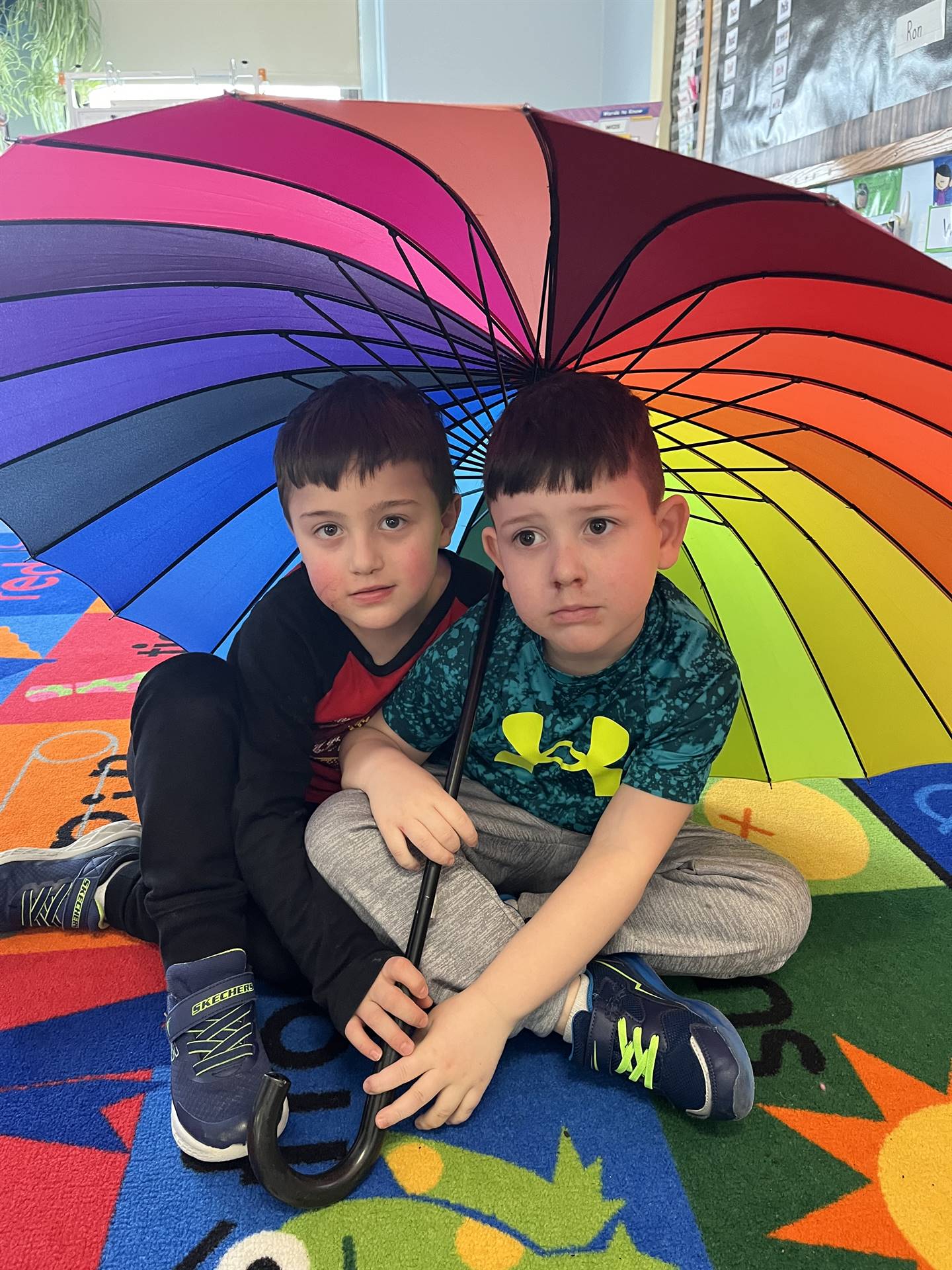 2 students sitting under a rainbow umbrella