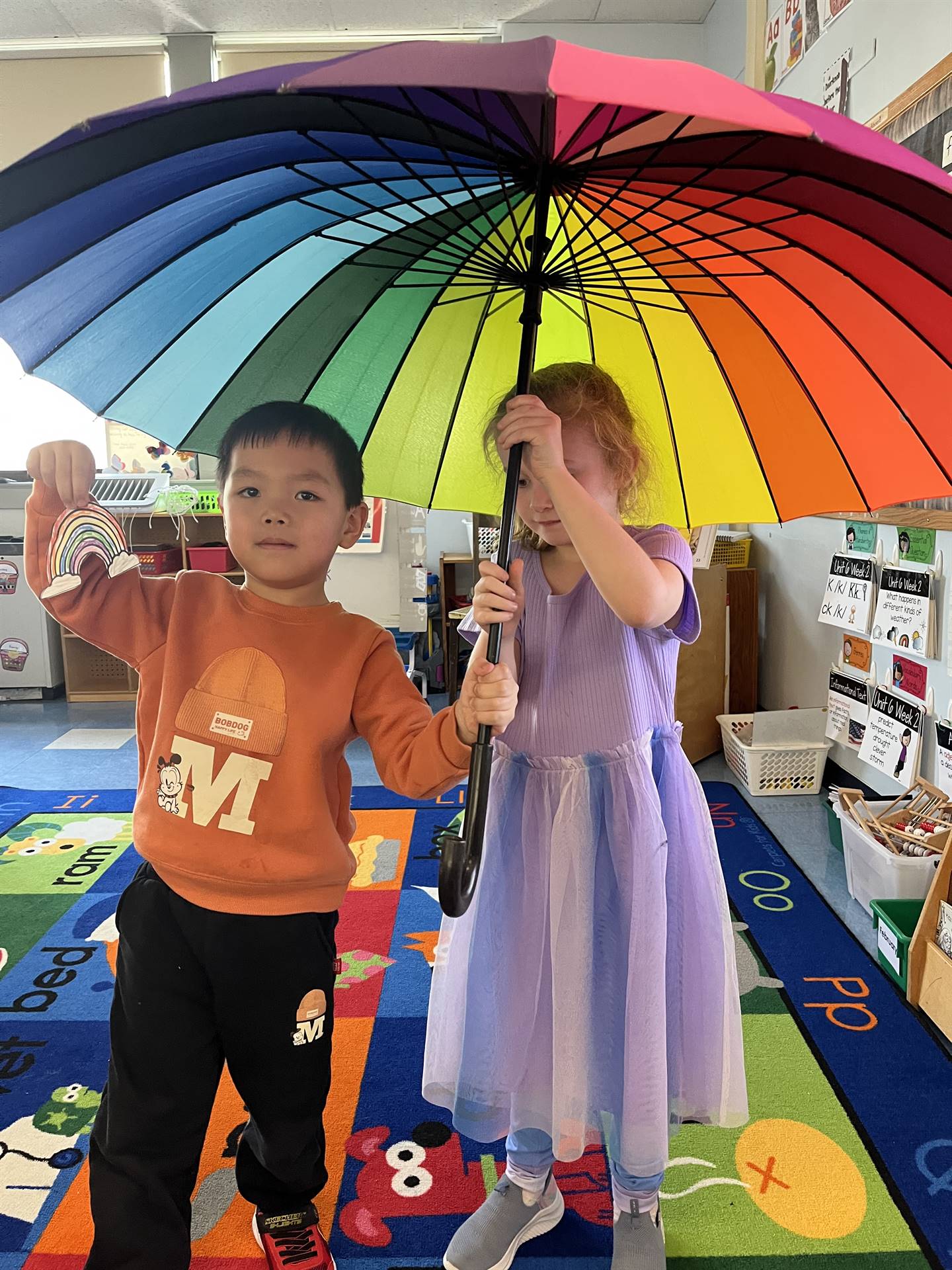 2 students sitting under a rainbow umbrella