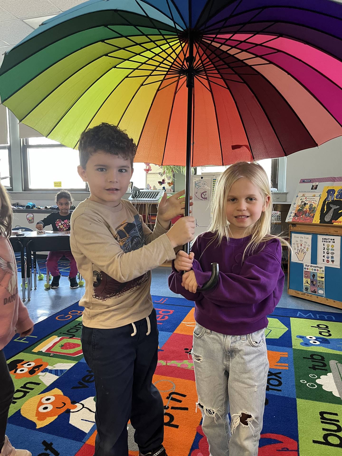 2 students sitting under a rainbow umbrella