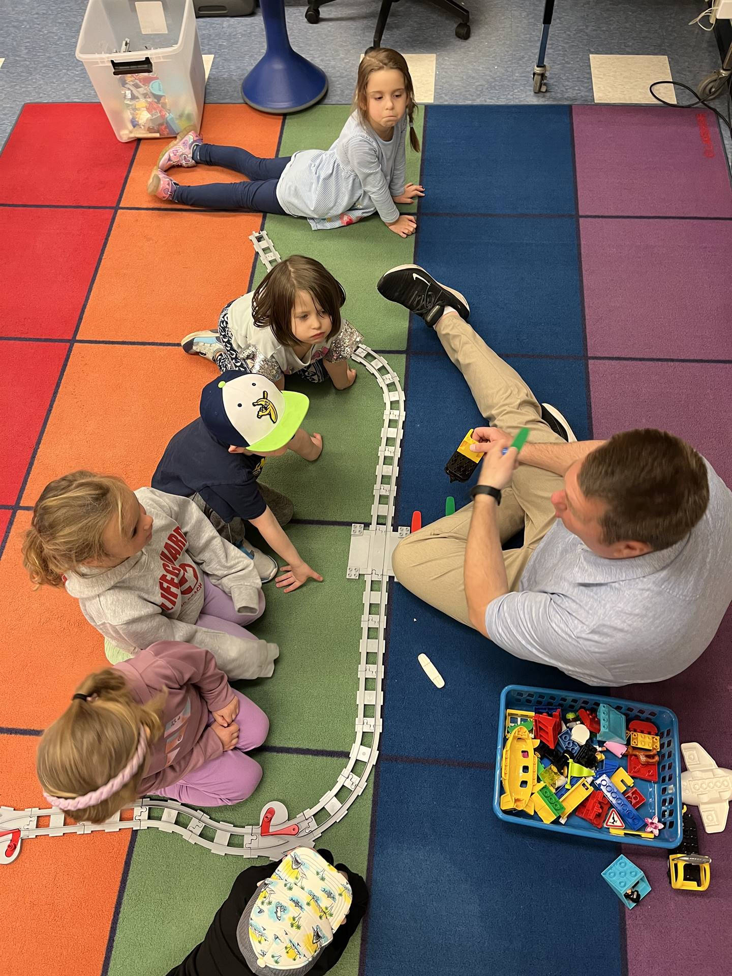 A teacher works with students to build a robot train track. 