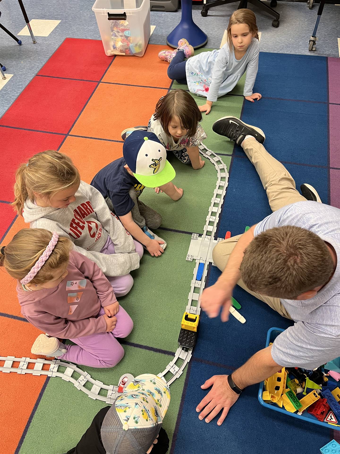 A teacher works with students to build a robot train track. 
