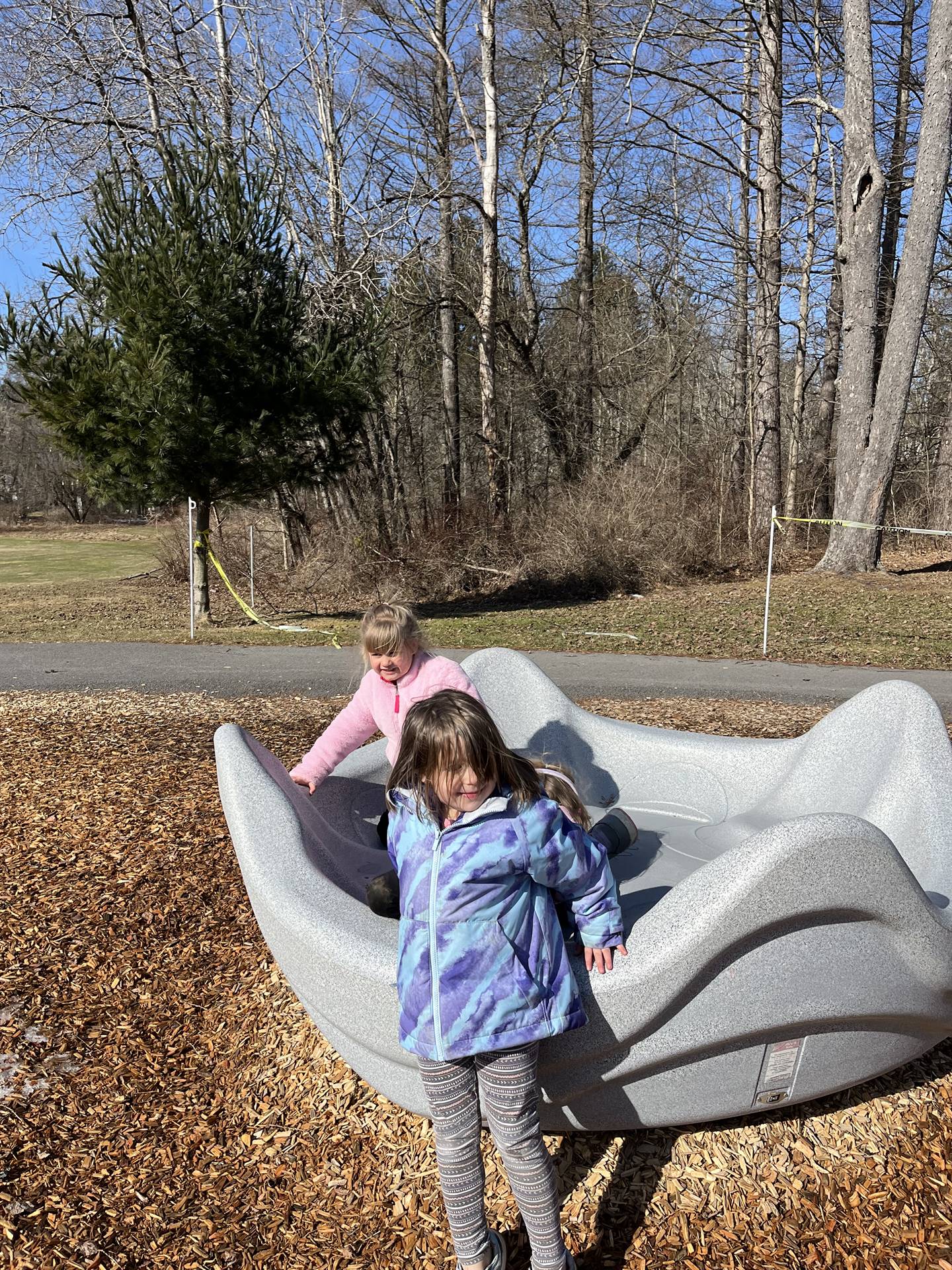 2 students on spin playground equipment outdoors.