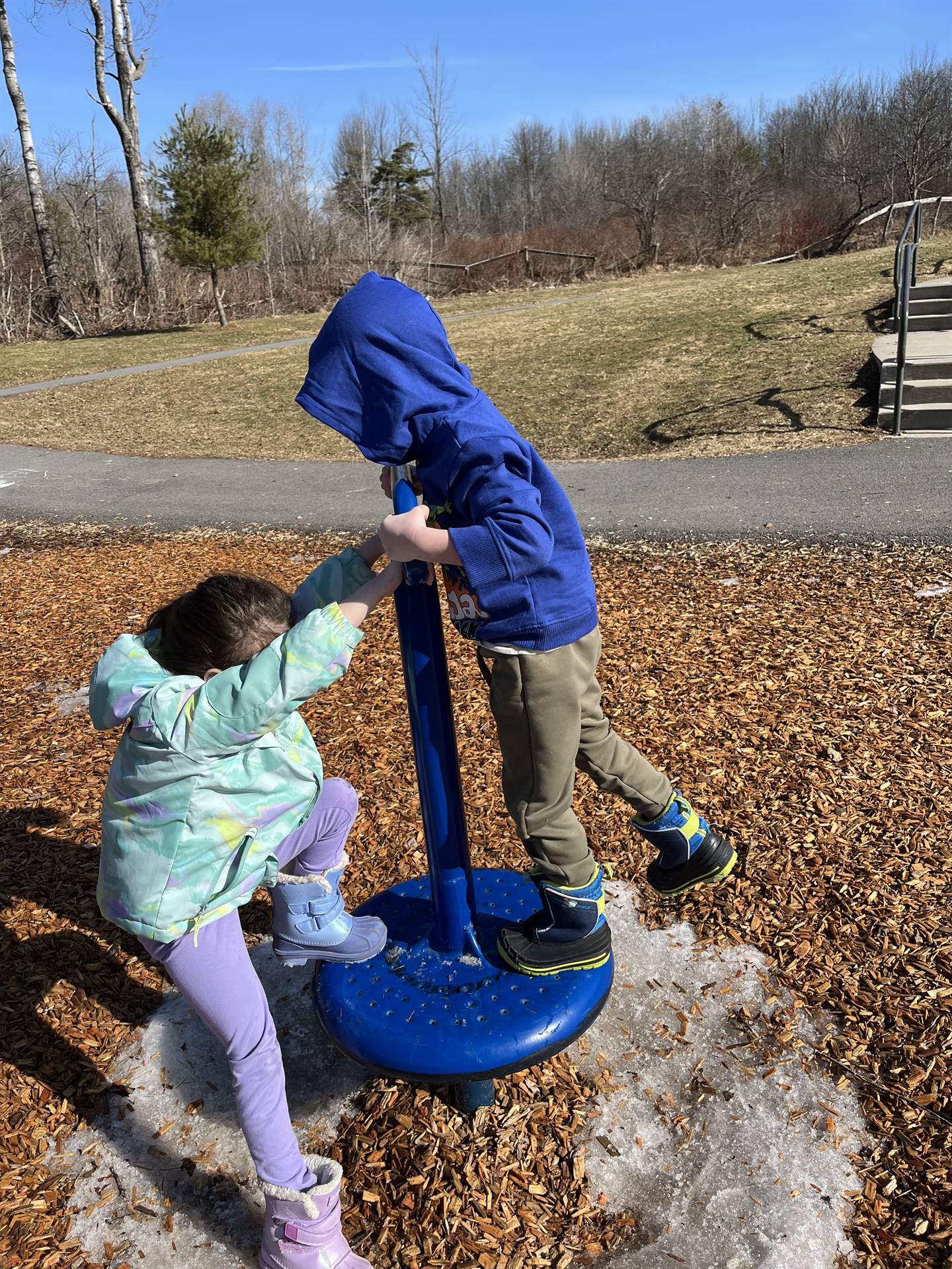 2 students on spin playground equipment outdoors.